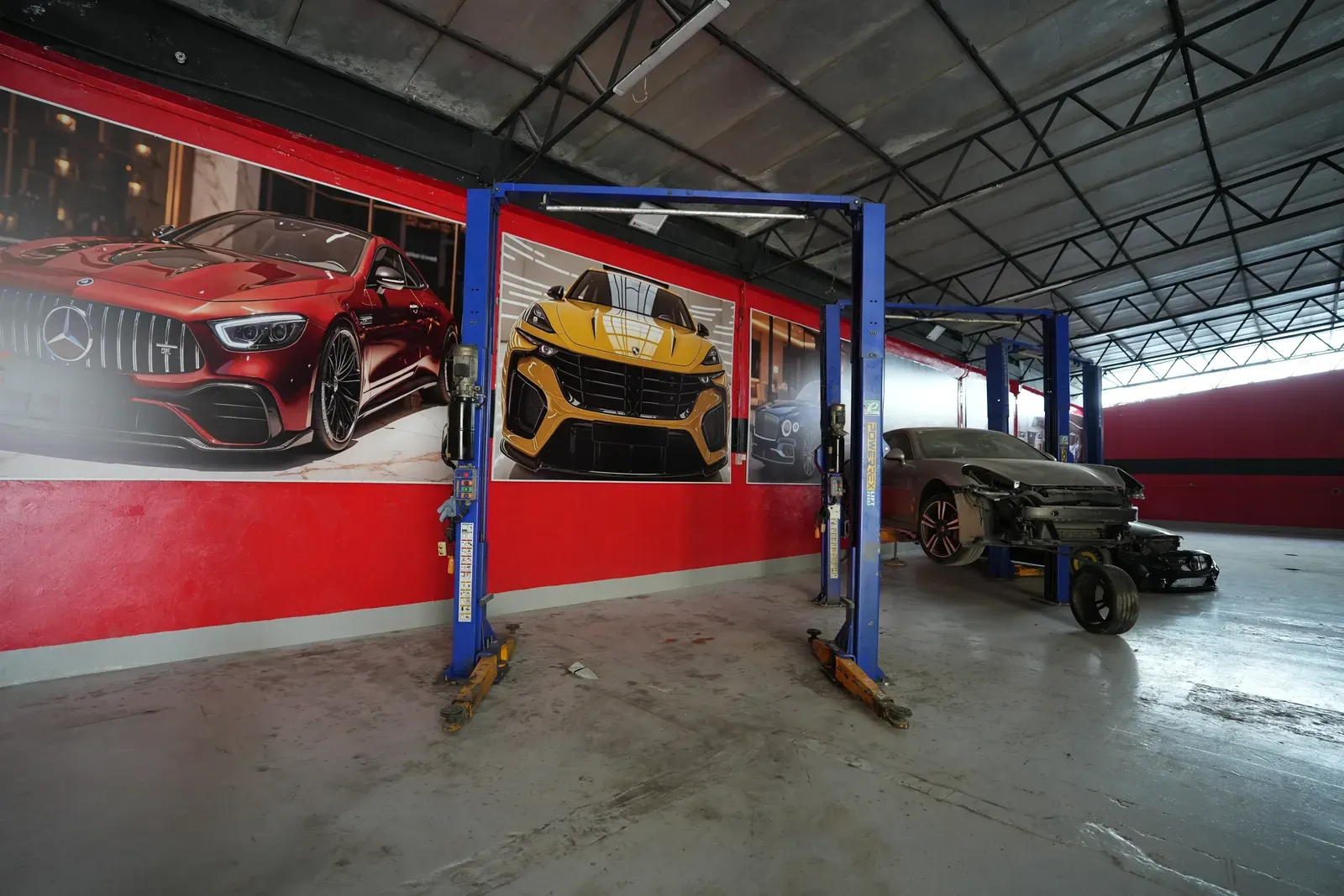 Two empty blue two-post lifts in front of the red workshop wall.