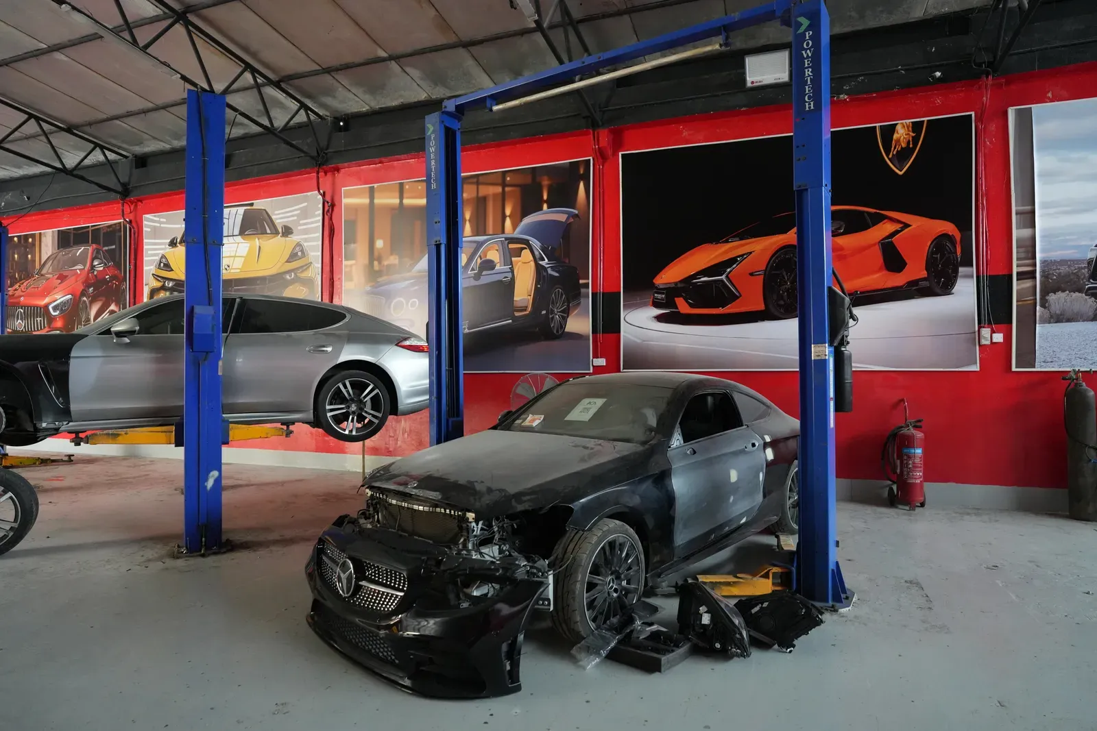 Two cars raised on blue two-post lifts, with a stripped coupe in front of them.