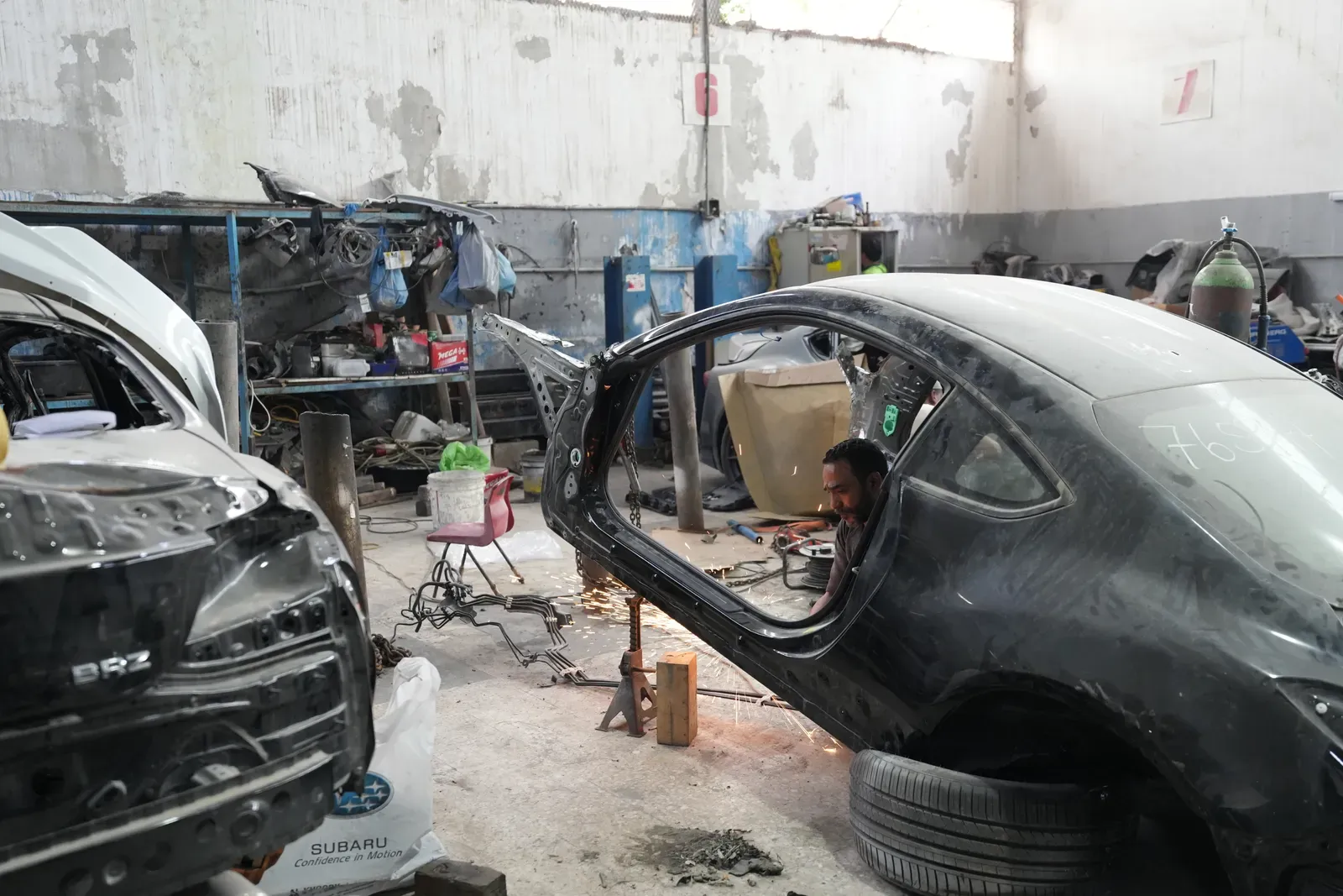 A car in the body shop with a door removed and a panel finished in primer.