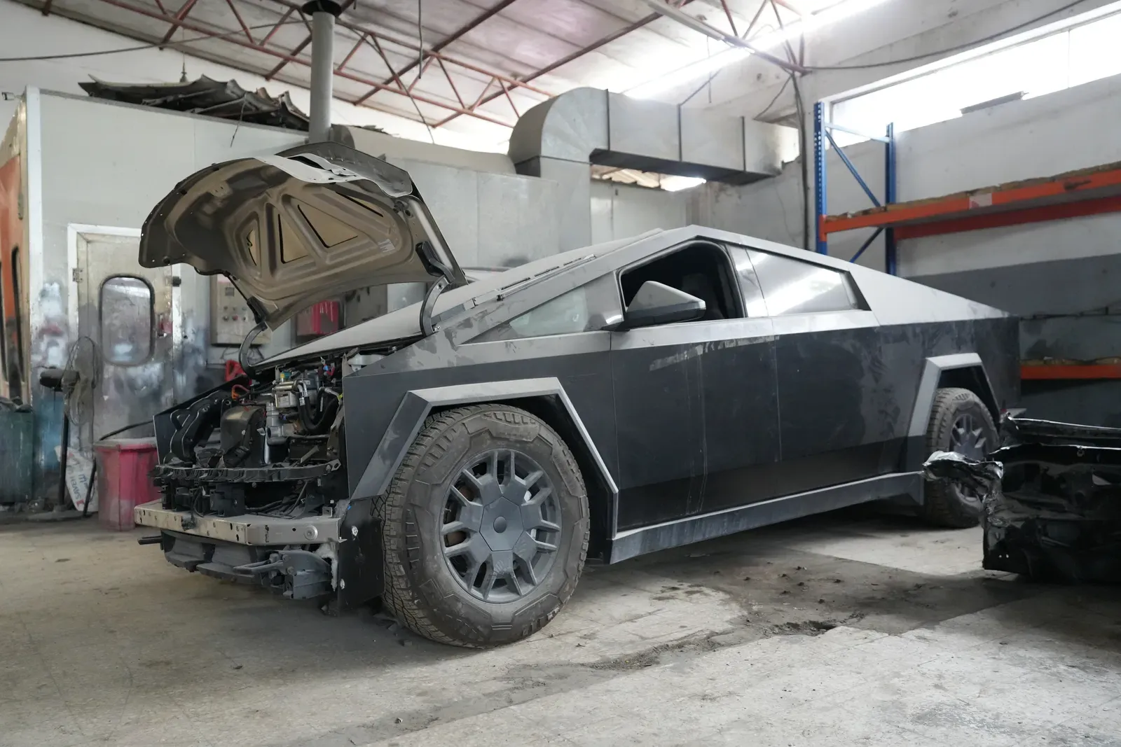 A vehicle standing in the workshop bay with its bonnet up and the front end stripped.