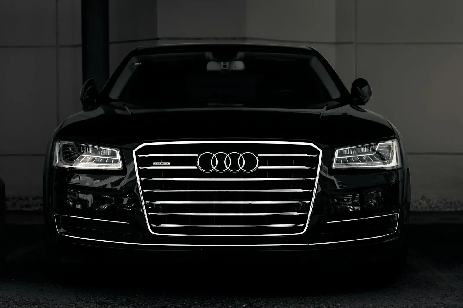 A black Audi A8 head-on, its grille and headlights coming out of near-darkness.