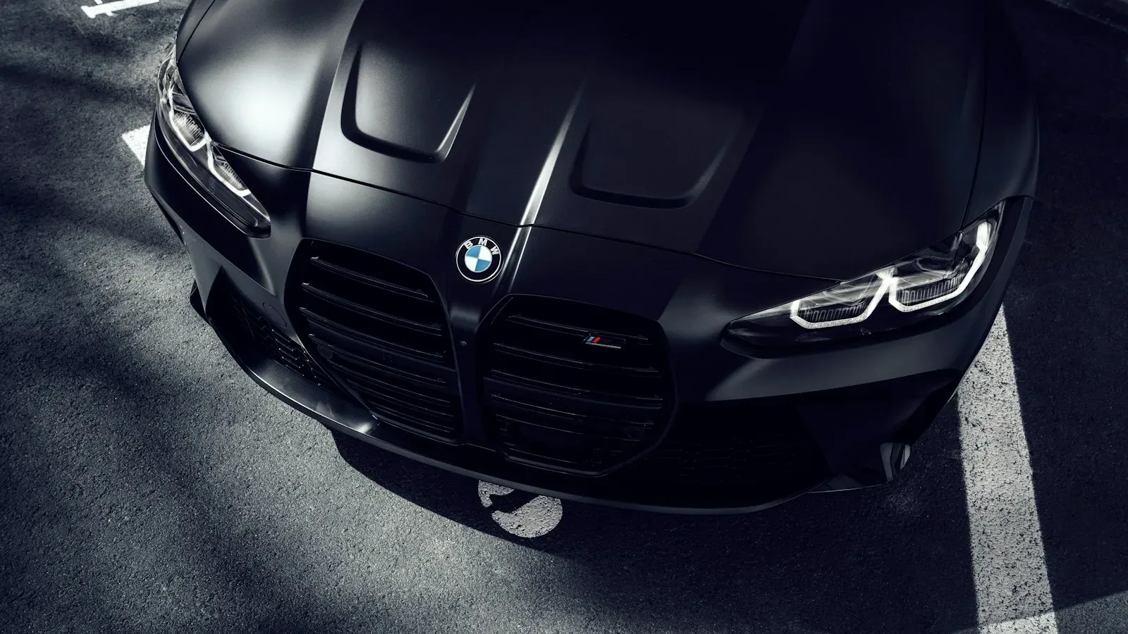 A matte black BMW M4, photographed close on the bonnet and grille in deep shadow.