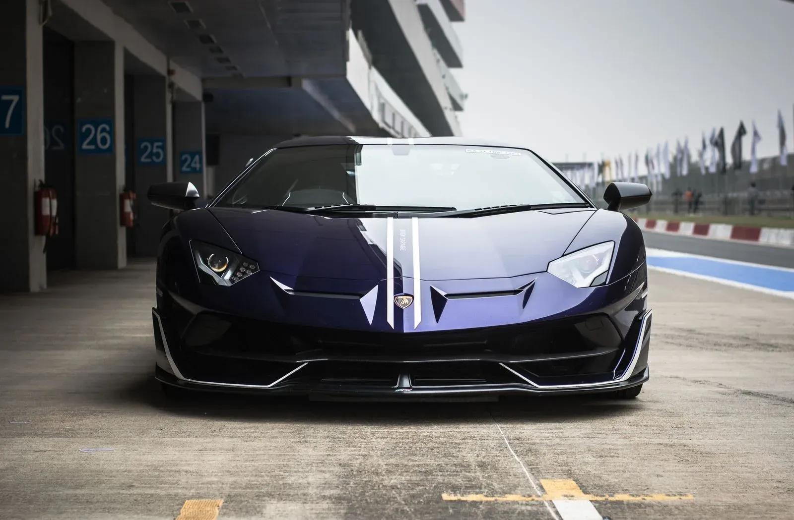 A dark Lamborghini Aventador SVJ photographed low and head-on in a pit lane.