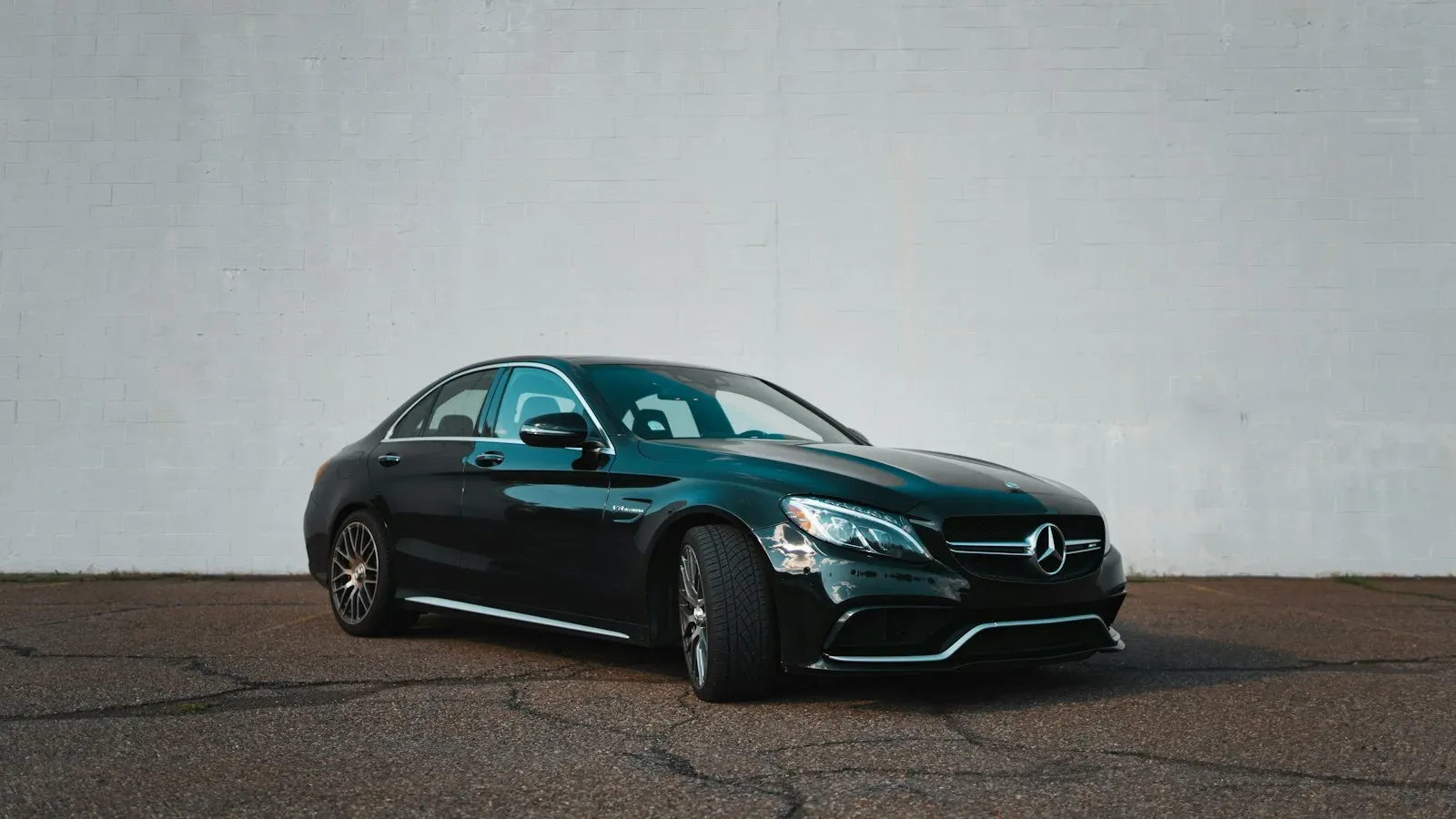 A black Mercedes-AMG C 63 against a plain wall, front three-quarter.